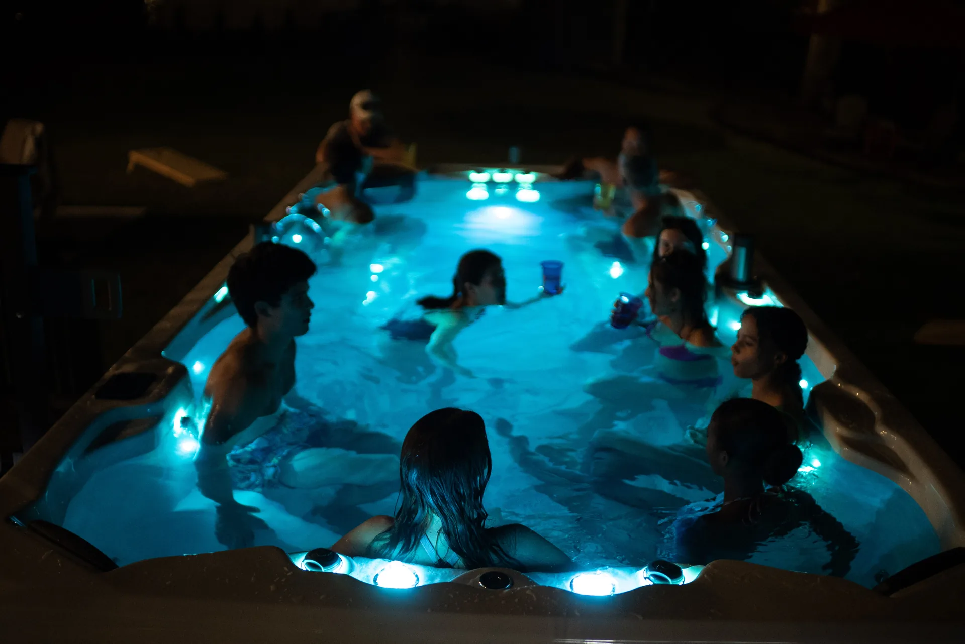 An Aspen swim spa lit up at night with a group of people in the water