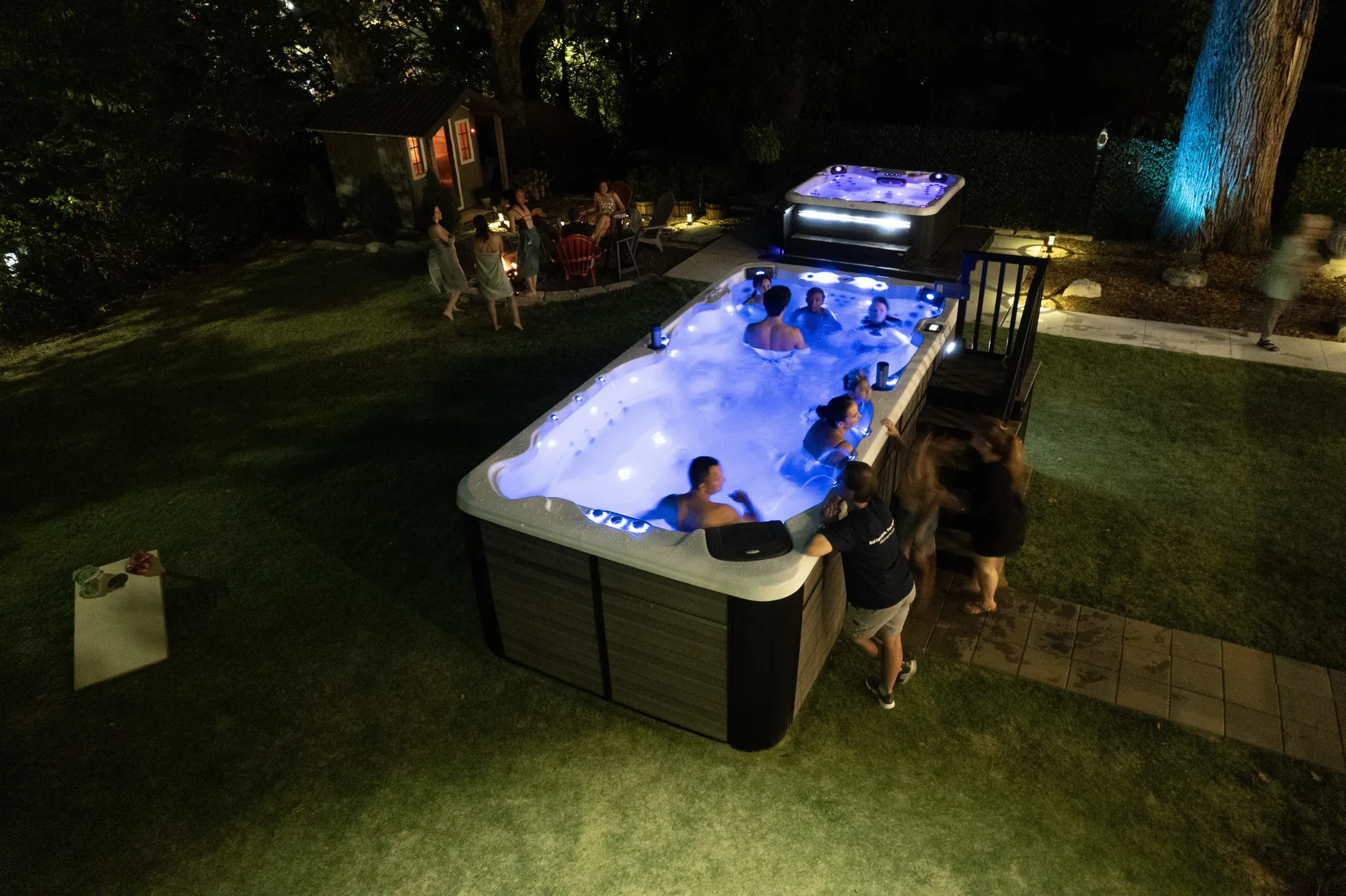 A lit Aspen swim spa in a backyard at night, seen from above
