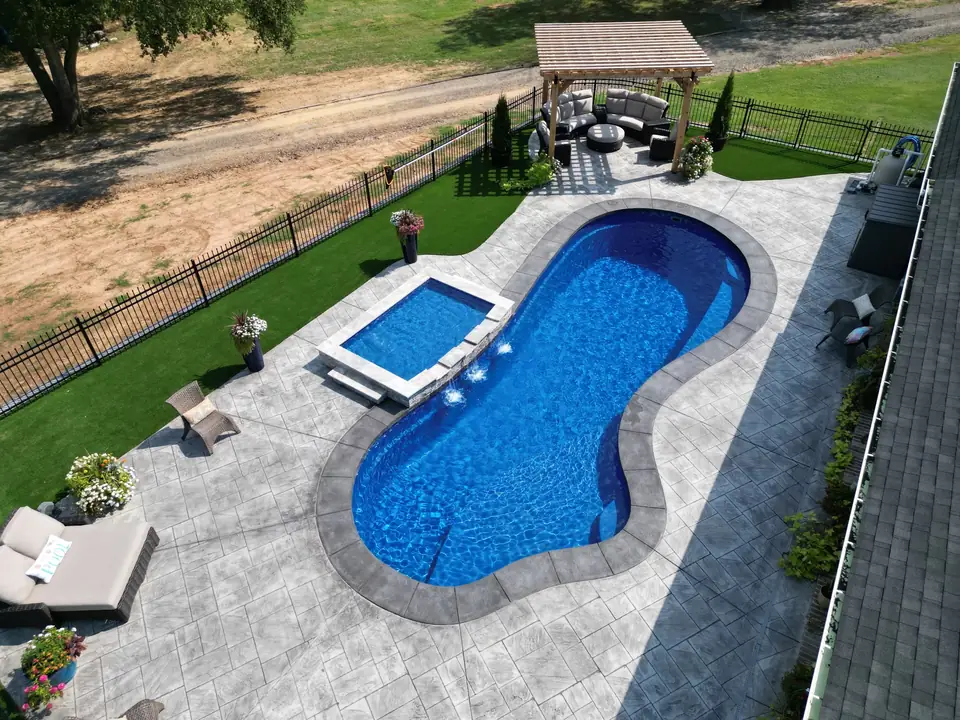 Freeform fiberglass pool with an attached raised spa, deck jets and a pergola seating area
