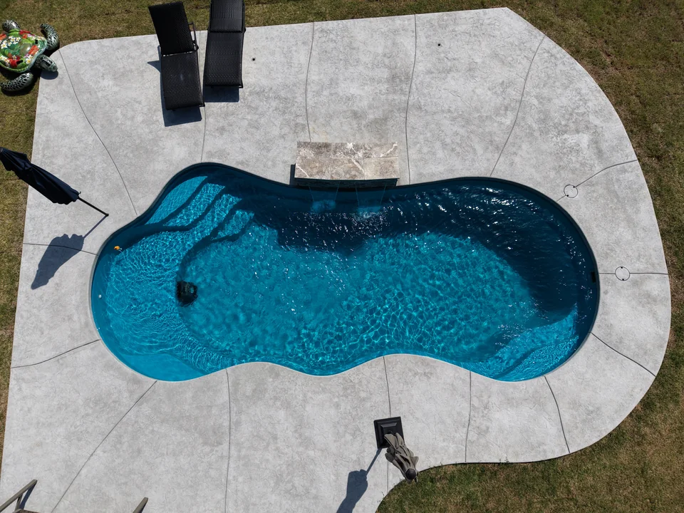 Freeform fiberglass pool with teal water and a raised travertine water feature with two spillways