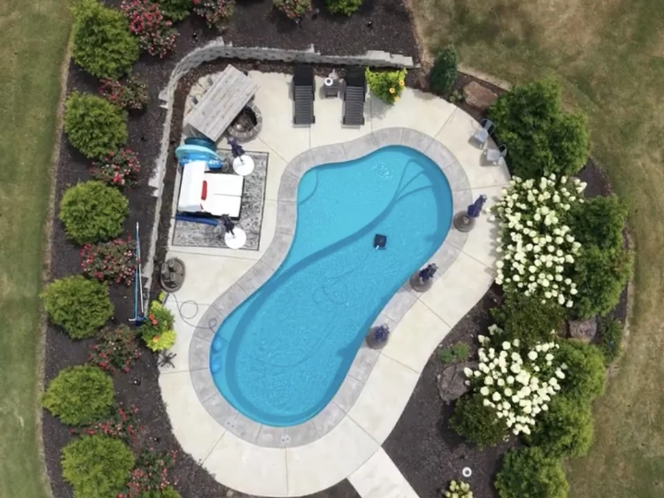 Aerial view of a landscaped fiberglass pool with a fire pit and pergola