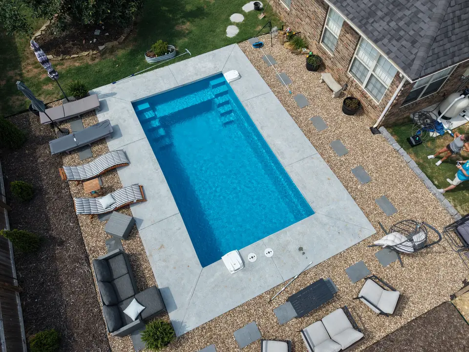 Overhead view of a rectangular fiberglass pool with a tanning bench and paver decking