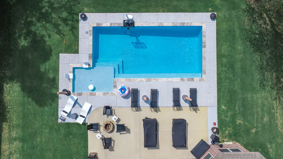 Overhead view of a rectangular fiberglass pool with an attached spa and travertine decking
