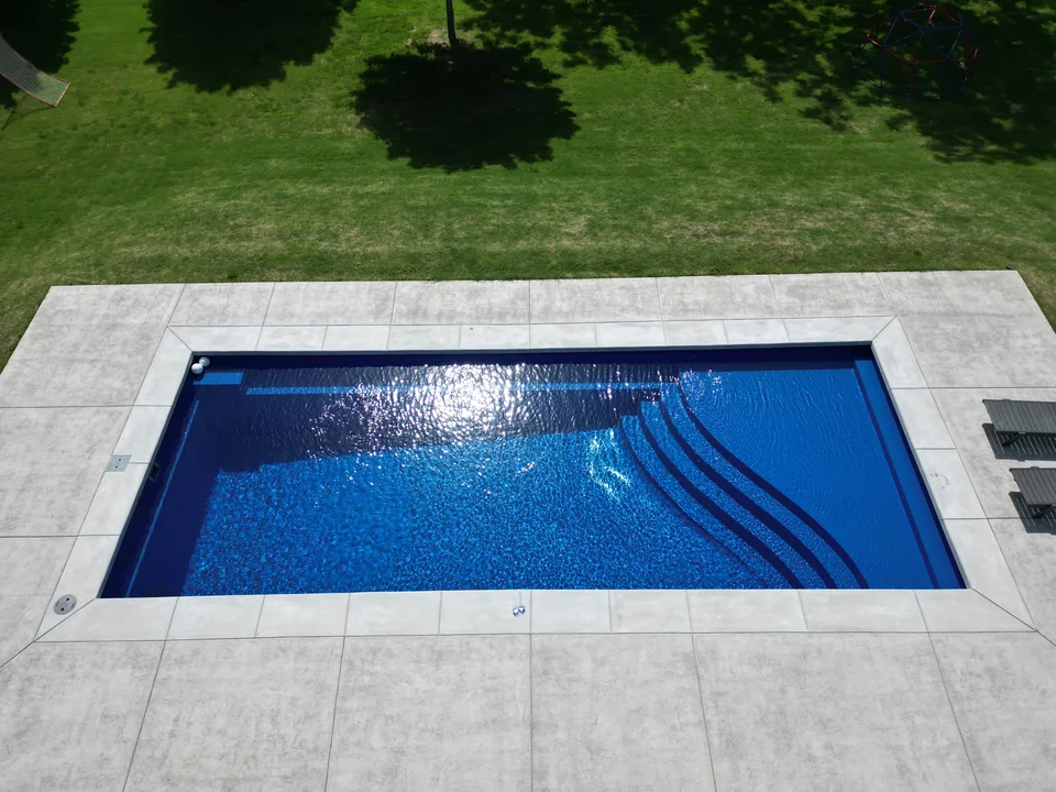 Rectangular fiberglass pool in Arkansas with deep blue water, full width entry steps and a bench along one side, set in a stamped concrete deck