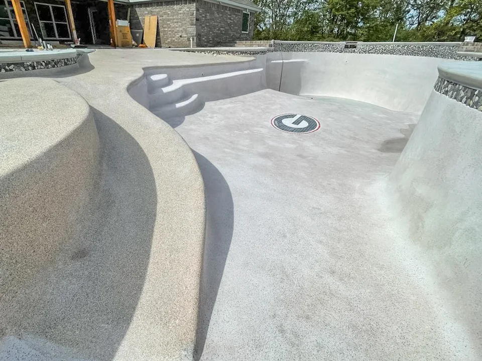 Gunite pool under construction in Fort Smith, Arkansas, showing the sprayed concrete shell with its curved ledge, steps, deep end and tile medallion before the interior finish and concrete decking are installed